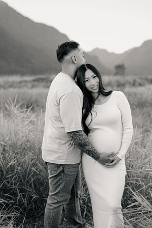 A couple embraces in a field at sunset, capturing intimate black and white maternity photos in nature.