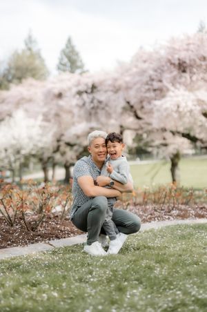 A touching moment captured at a cherry blossom park with blooming pink trees creating a dreamy spring backdrop.
