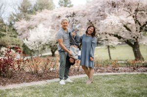 A couple stands together on grass with blooming cherry blossom trees creating a romantic spring backdrop.