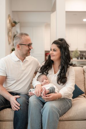 A couple sitting on a couch at home sharing tender moments with their newborn baby in a series of candid photos.