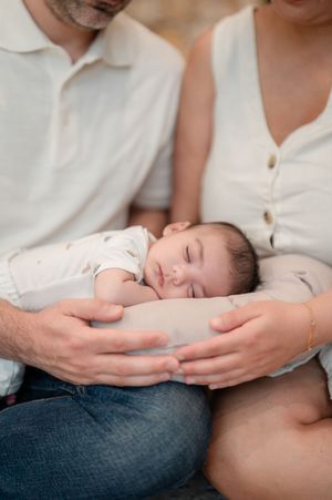 A tender moment showing hands cradling sleeping newborn baby swaddled in white.