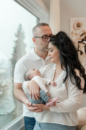 Family shares tender moments near a window in an intimate lifestyle photography series showing parent and baby bonding.