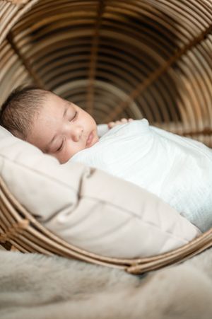 Close-up view of sleeping infant in white swaddle resting in curved wicker basket.