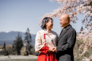 Happy couple sharing a romantic moment under blooming cherry blossoms with mountains in the background.