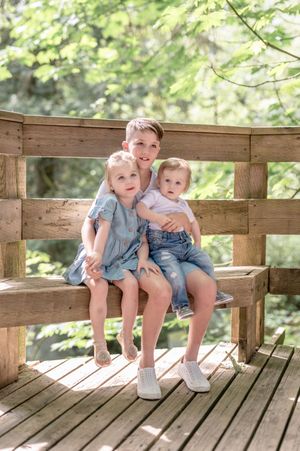 Three children sit together on a wooden deck platform in similar denim outfits.