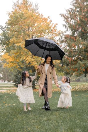 Two people in trench coats share black umbrellas while dancing together on autumn grass with golden trees in background.