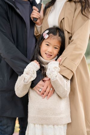 A child wearing a cream knit sweater with lace detail poses with adults in formal attire during a photo session.