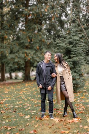 A couple shares tender moments in a park with autumn leaves scattered on the ground.
