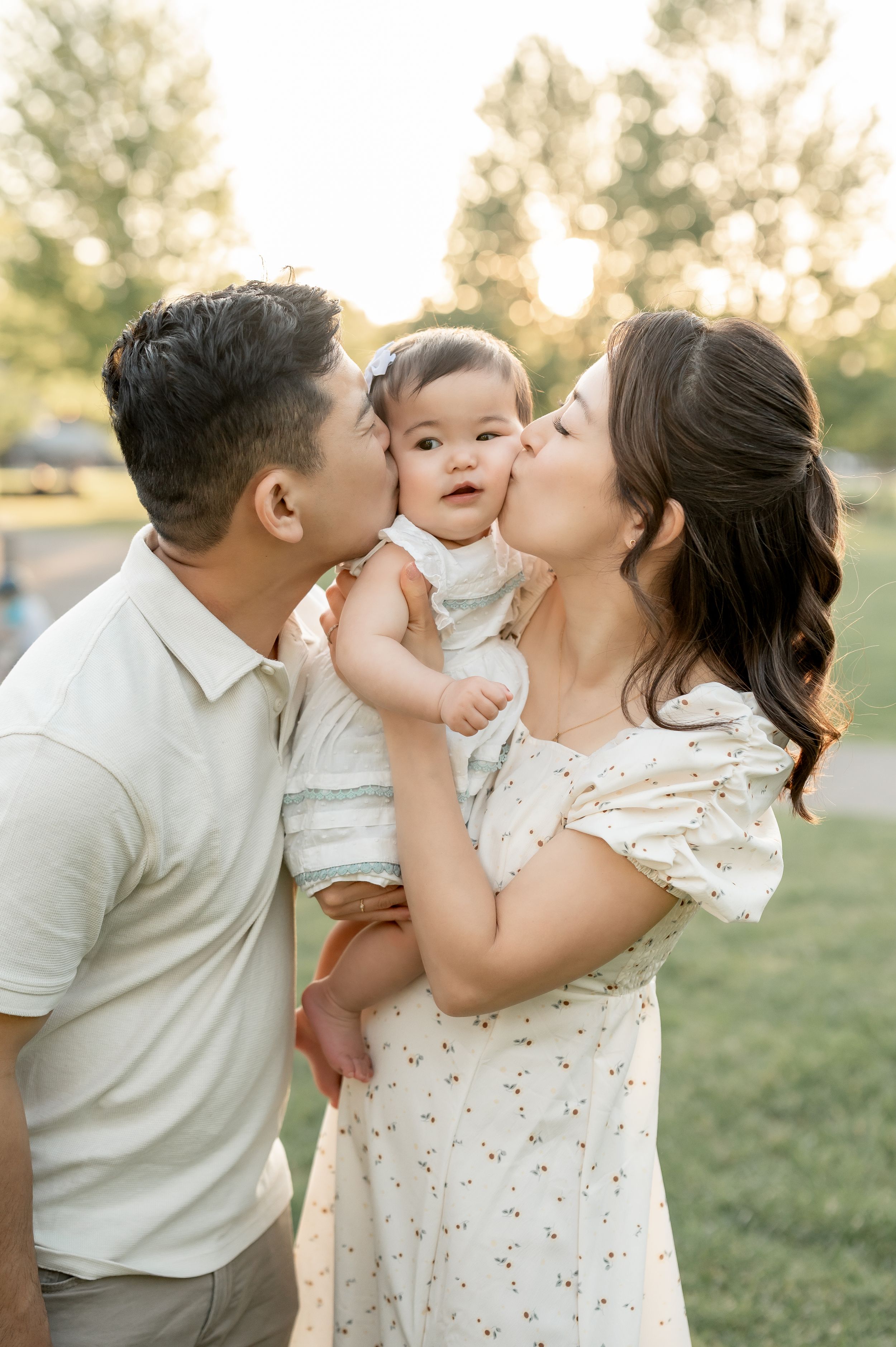 A couple kisses their baby girl on the cheeks during a golden hour family portrait session outdoors.