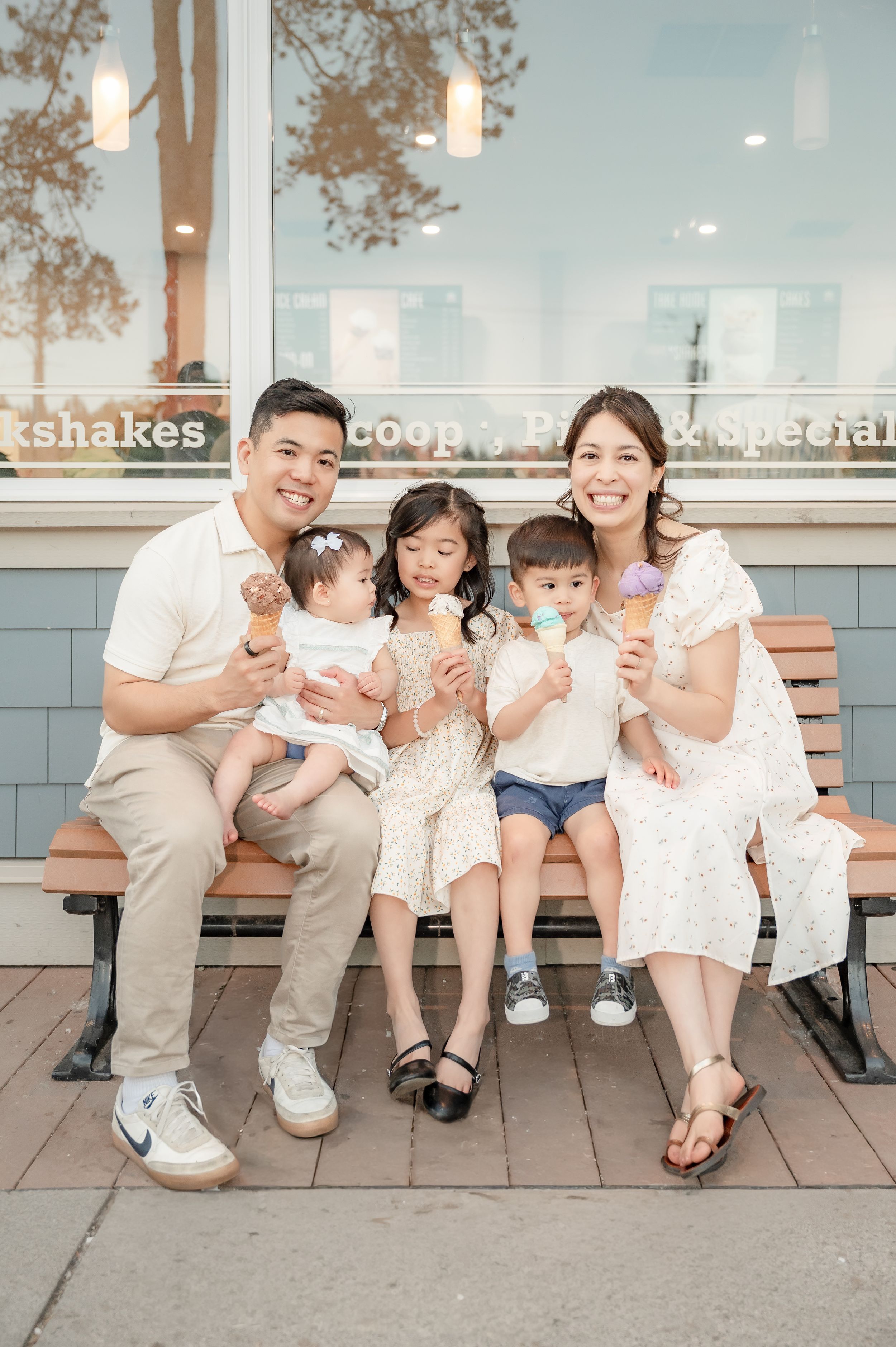 Happy Asian family of five enjoying ice cream cones on a bench outside an ice cream shop.