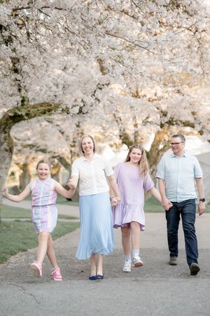 Family of four walking hand-in-hand under blooming cherry blossom trees in spring, wearing pastel outfits.