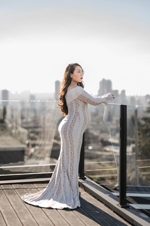 Woman in white lace dress poses on rooftop terrace with urban skyline backdrop during golden hour photoshoot.