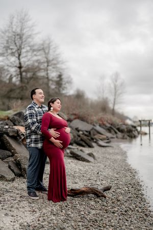 A couple embraces on a rocky beach shore under cloudy skies in a romantic photoshoot sequence.