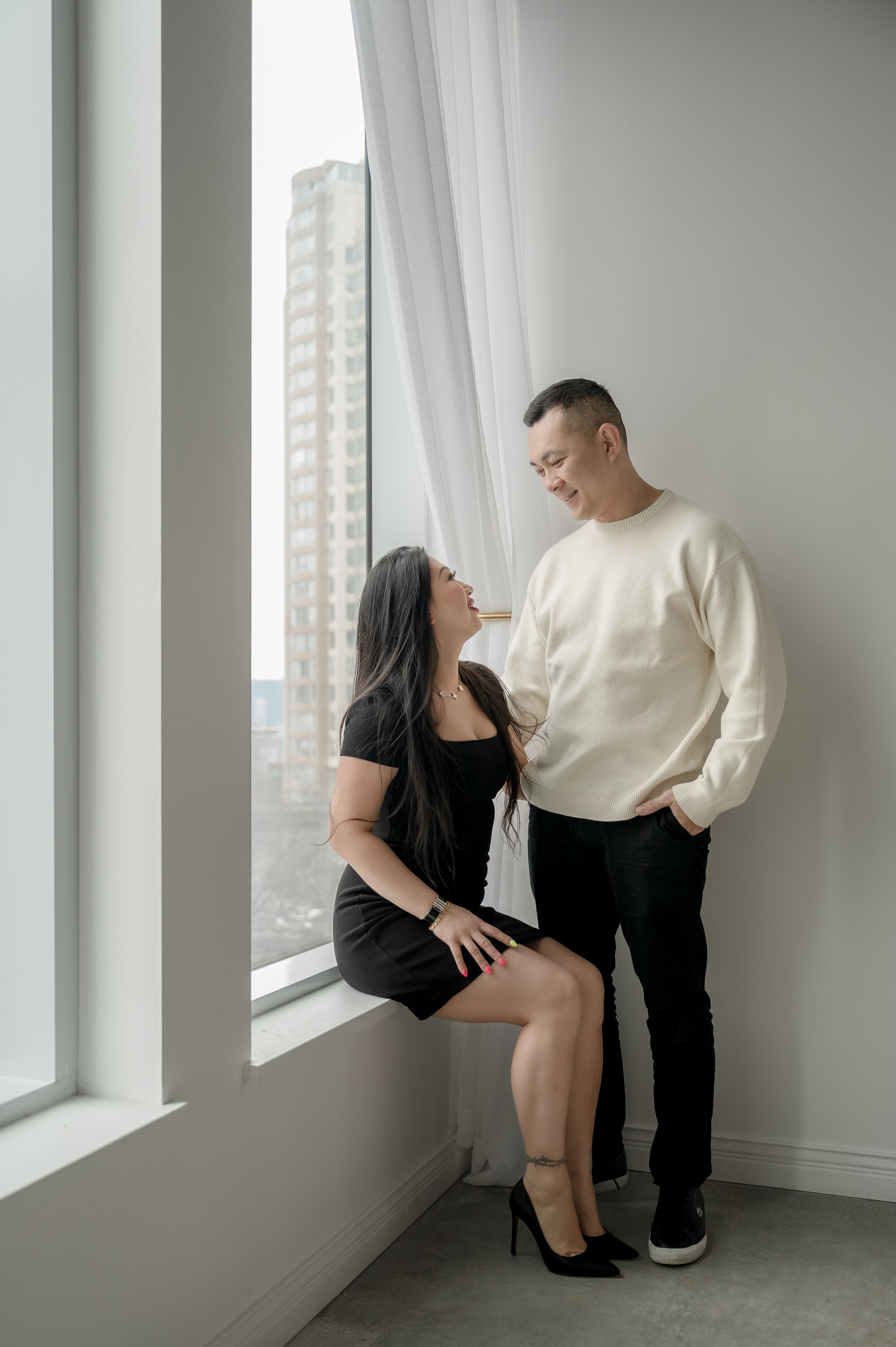 A couple poses intimately in three artistic black and white photographs by a bright window in a minimalist room.