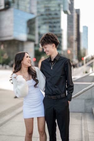A smiling couple shares a joyful moment together on a city street, with modern buildings in the background.