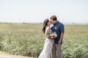 A romantic couple embraces in a wind-swept wheat field during sunset, creating a dreamy golden hour moment.