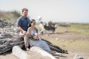 A couple shares a romantic moment on the rocky seaside while holding a flower bouquet in their hands.