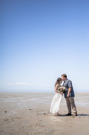 A couple shares a romantic moment on a sandy beach with clear blue skies in the background.