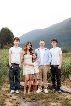 Family portrait outdoors with mountains and tall grass in scenic natural setting during golden hour.