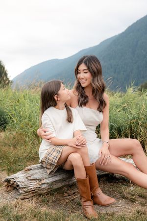 A tender moment shared between two people sitting on a log against a backdrop of misty mountains and tall grass.