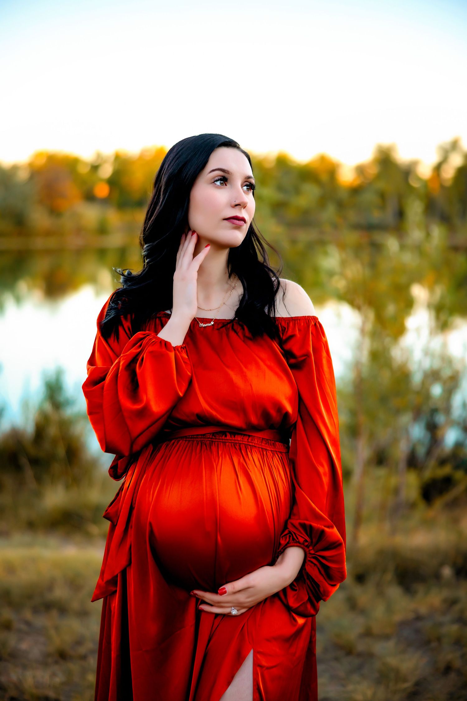A dramatic maternity portrait featuring a red dress against a large tree trunk at sunset. Pueblo Photographer
