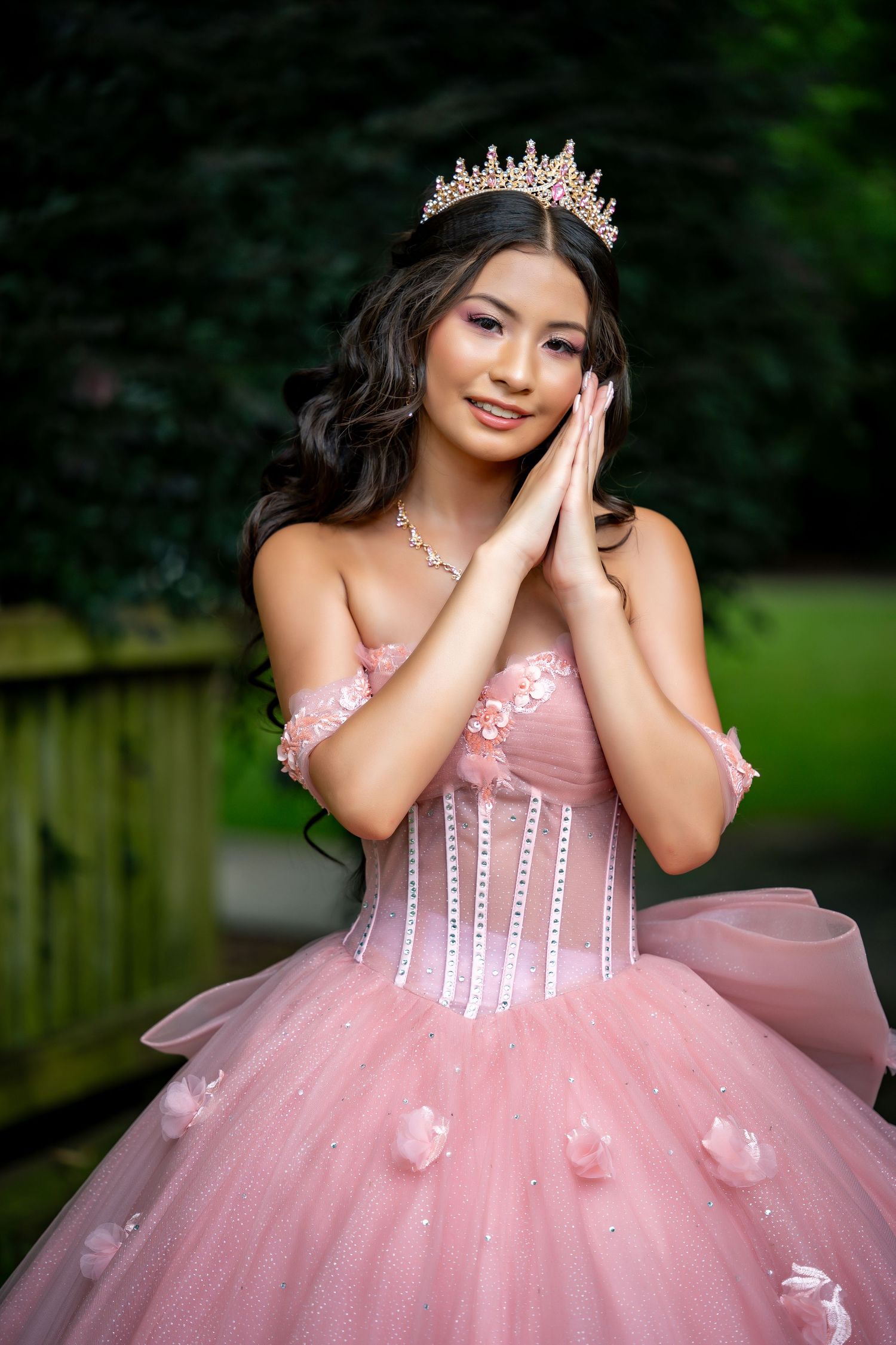 A woman in a sparkling blue ball gown poses outdoors while holding a white bouquet.