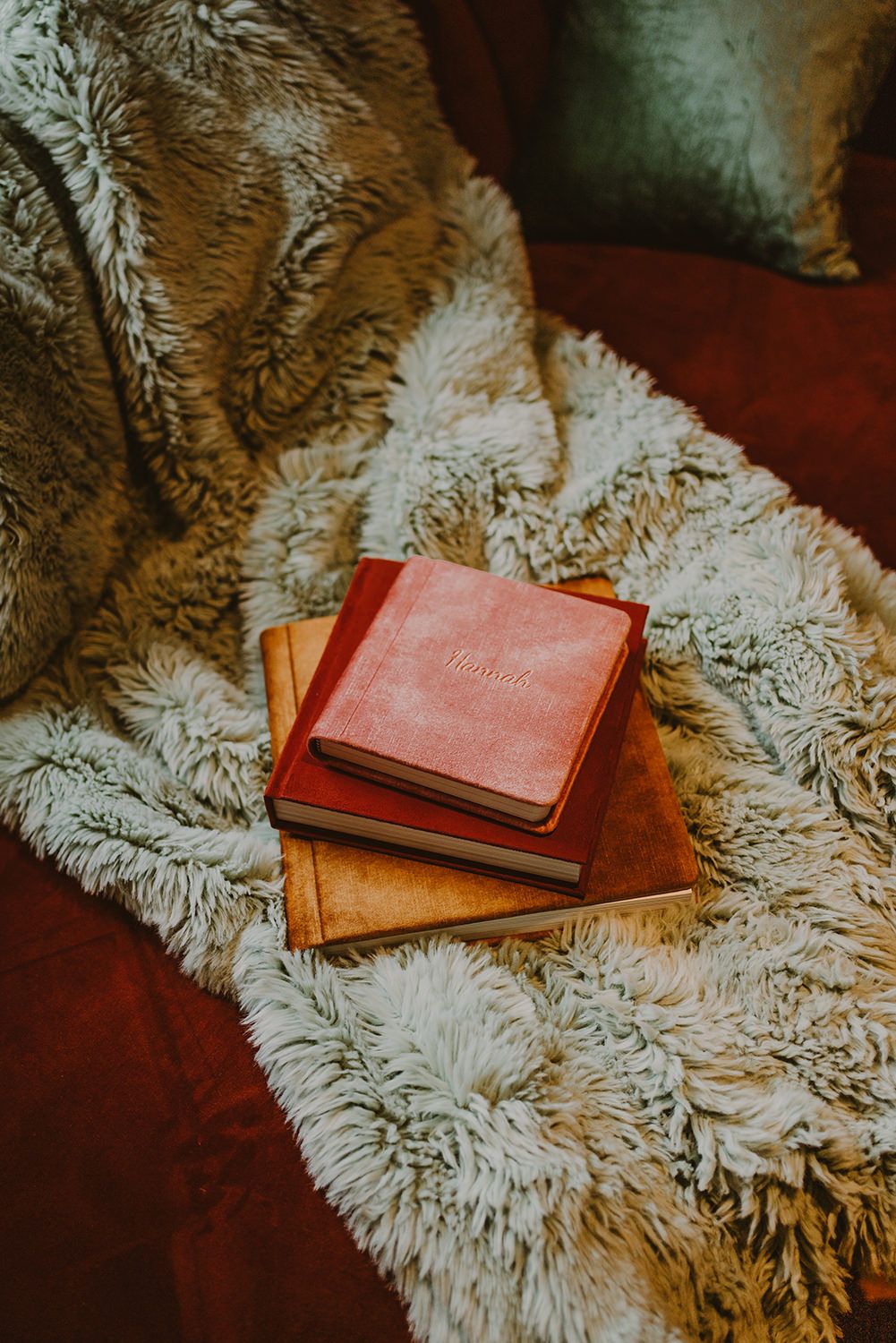 Stack of vintage books resting on plush white fur blanket against dark background.