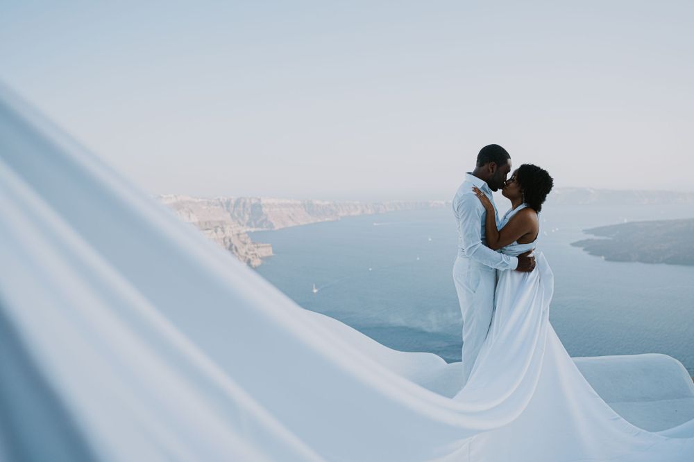 A romantic silhouette moment overlooking the Aegean Sea in Santorini with flowing white fabric.