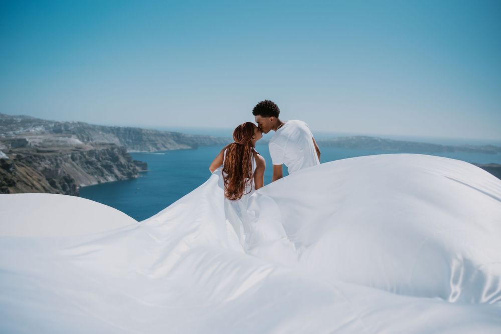 Couple embracing on white dome rooftop with Mediterranean backdrop.