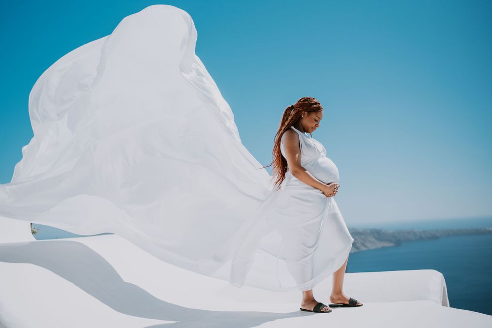 Flowing white dress billows dramatically against blue Mediterranean sky on Santorini's white architecture.