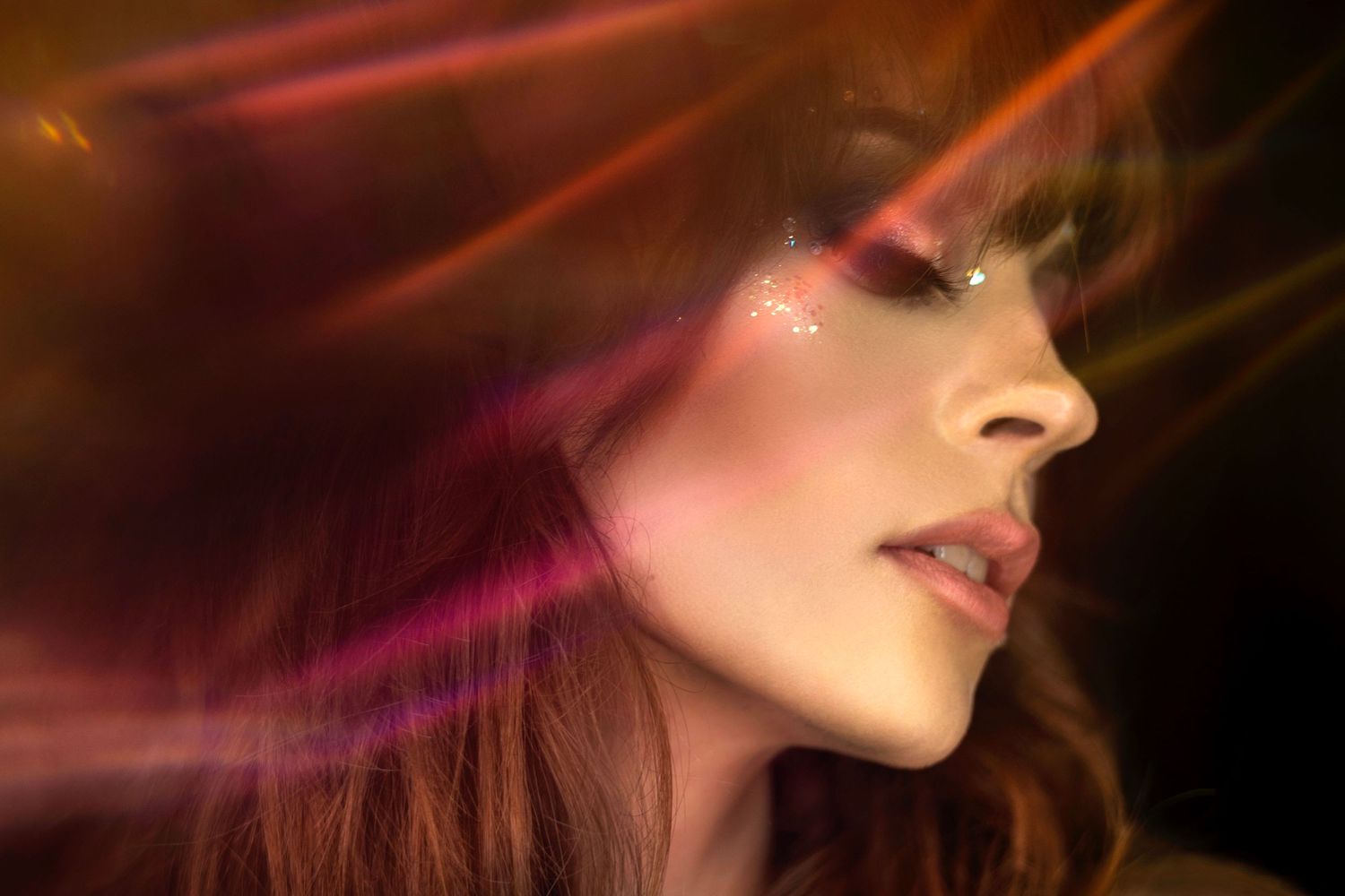 Abstract portrait with colorful light streaks creating dreamy atmosphere against dark background.