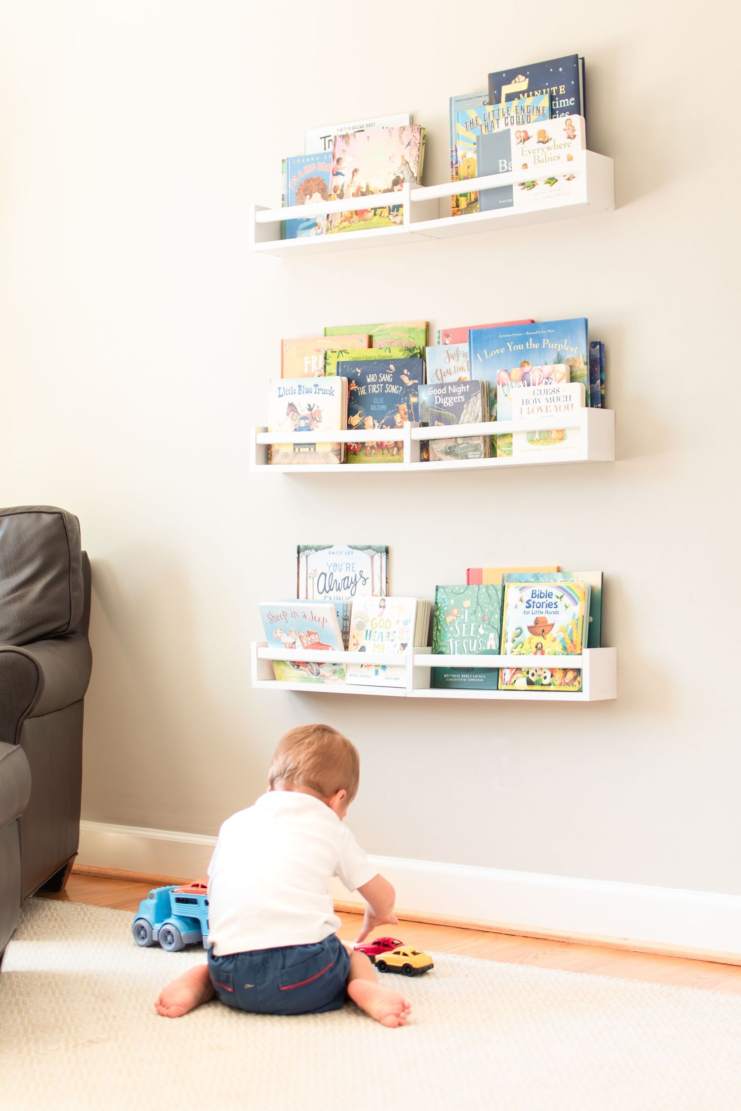 A young boy plays with cars below his assortment of books on the shelves of his room.