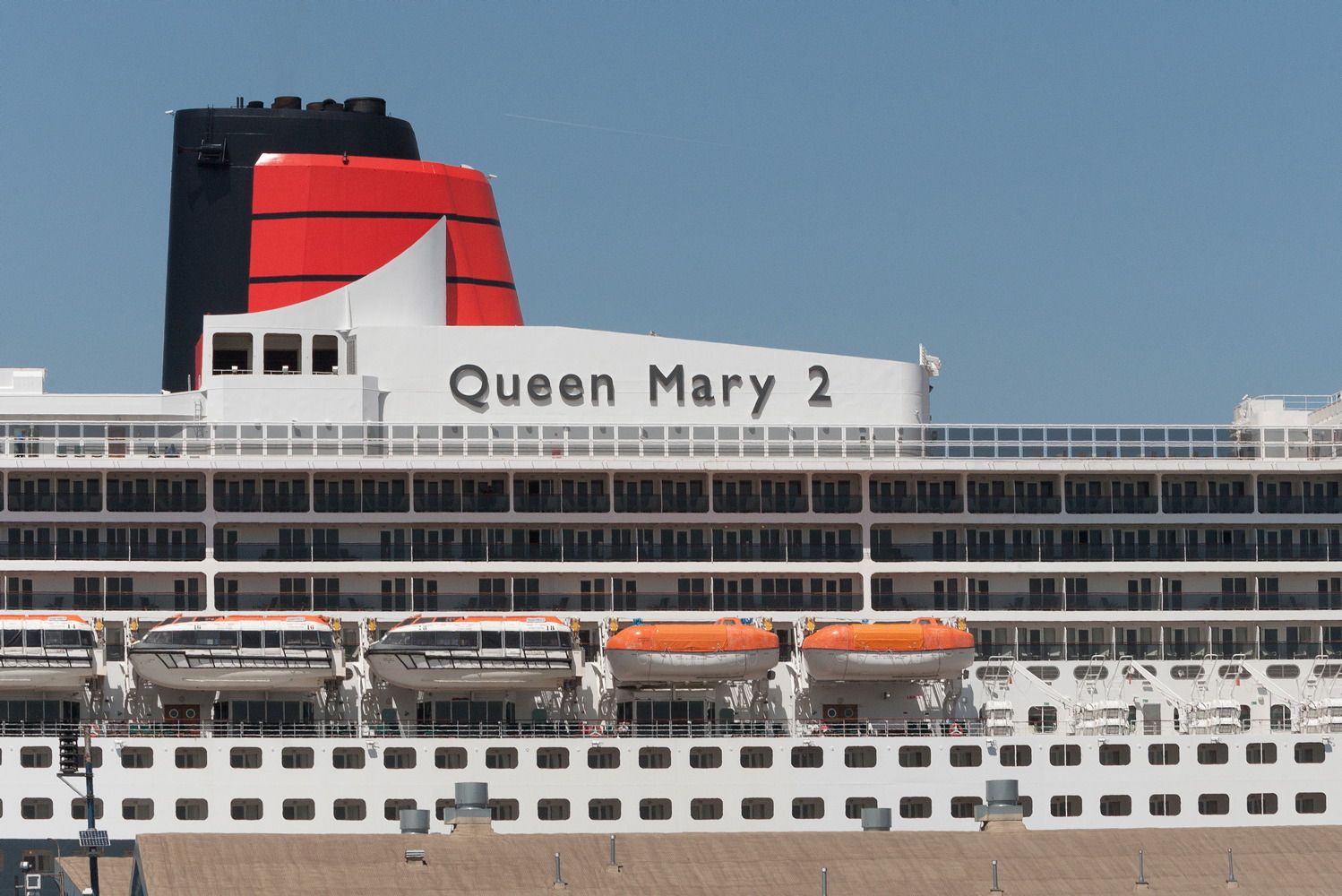 Side profile of Queen Mary 2 cruise ship showing distinctive red and black funnel design.