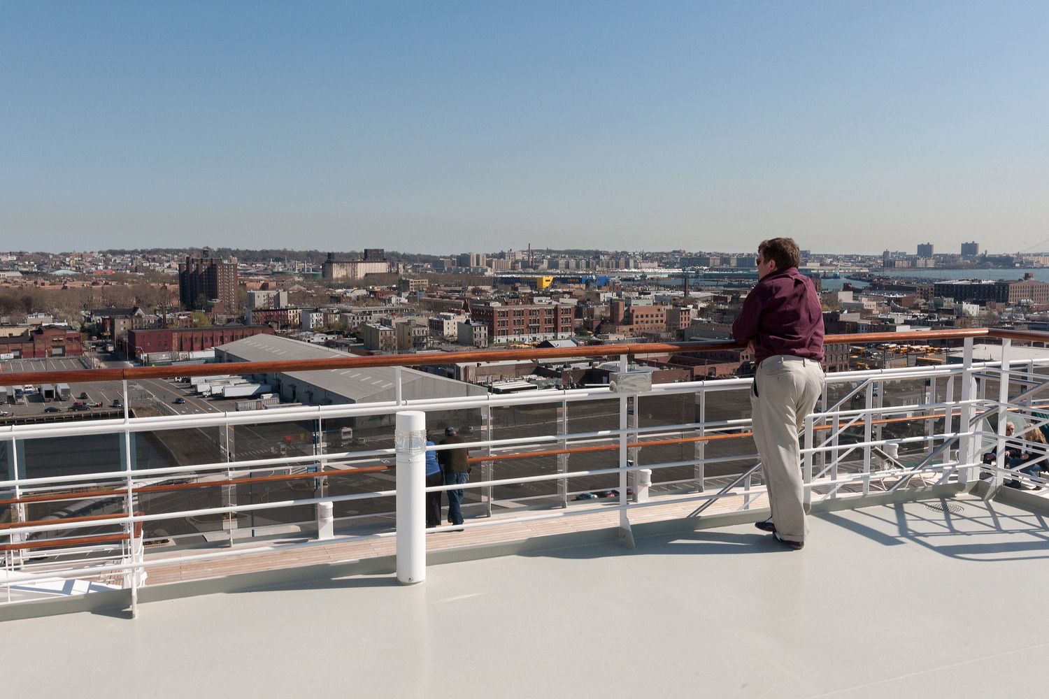 Panoramic view of a cityscape from a cruise ship deck railing on a sunny day.