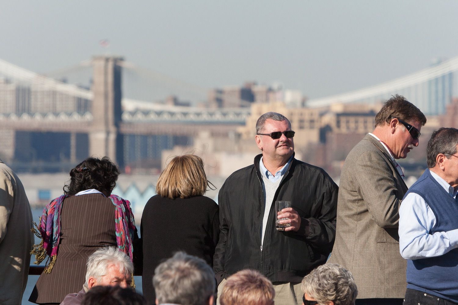 Passengers gathered on the deck of a cruise ship with city skyline in the background.