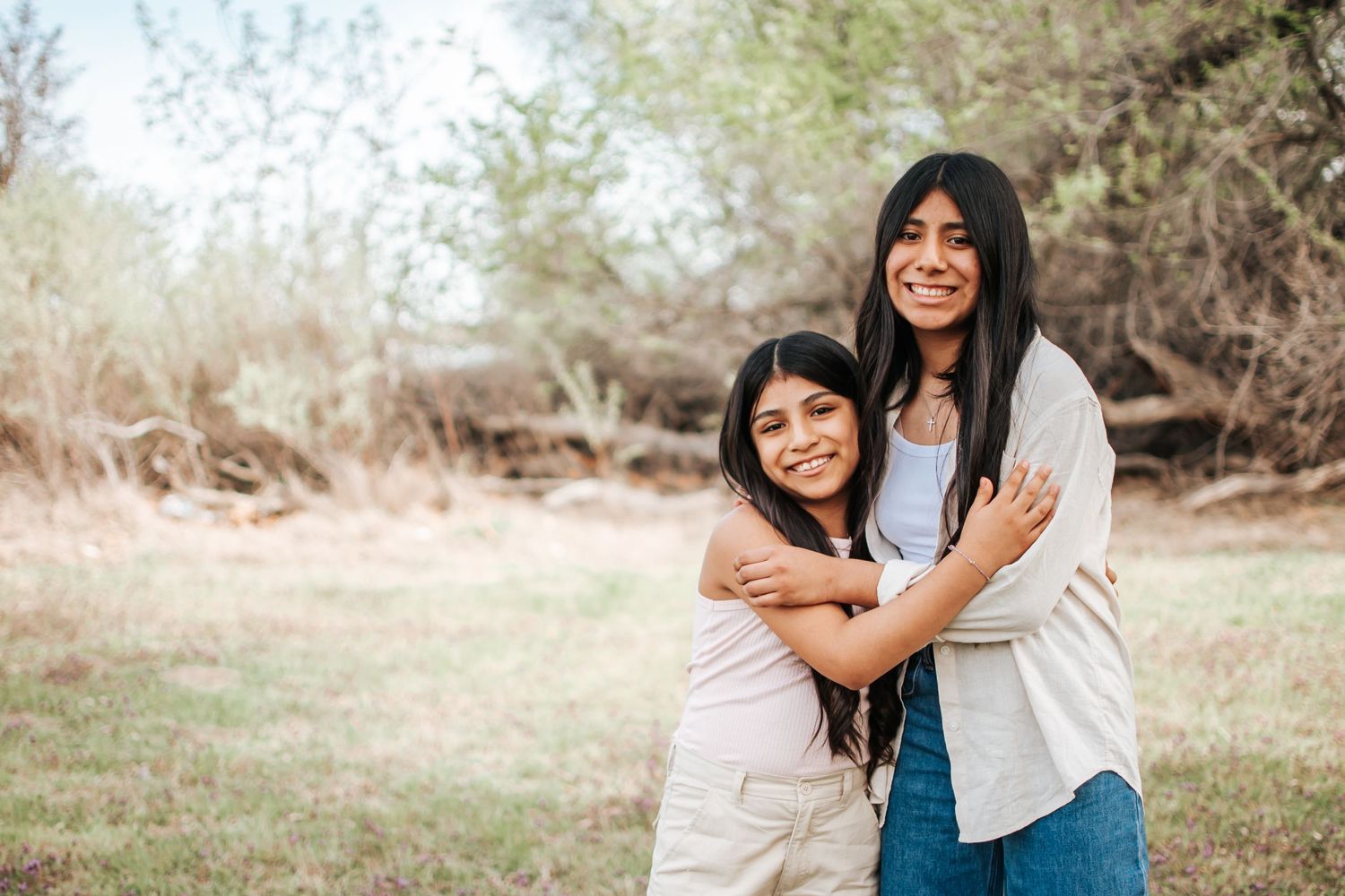 Two sisters embracing and laughing joyfully outdoors on a sunny spring day in Tri Cities, Washington.