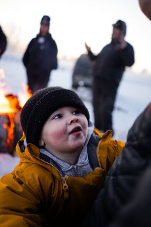 A child in a yellow winter coat looks up at the sky during a winter evening.