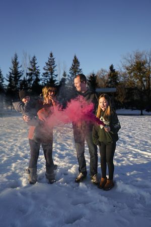 People playing with pink smoke bombs in a snowy field on a sunny winter day.