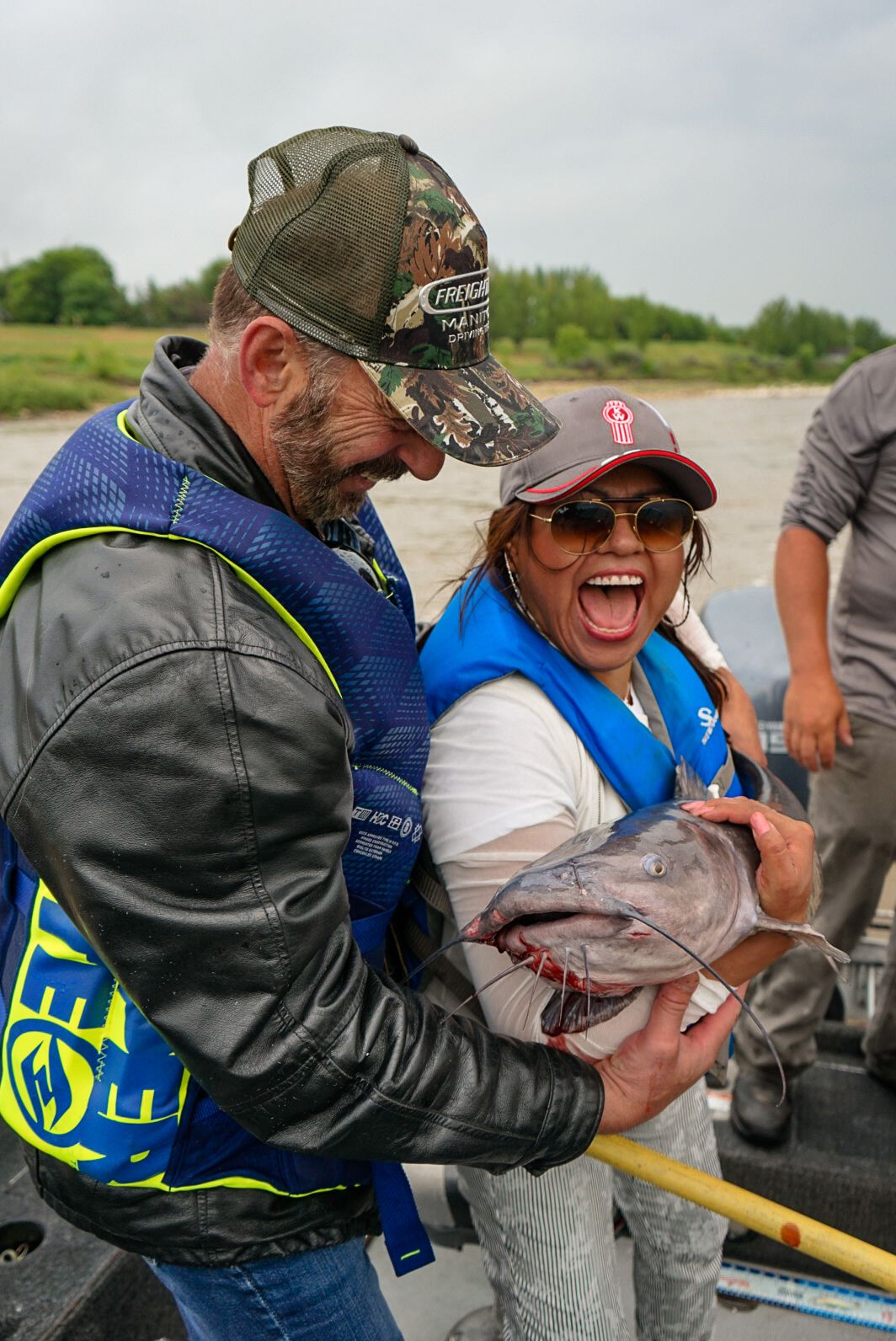 People in life vests laughing while holding freshly caught fish.