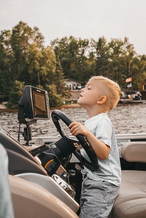 Young child pretending to drive a boat while sitting at the steering wheel.