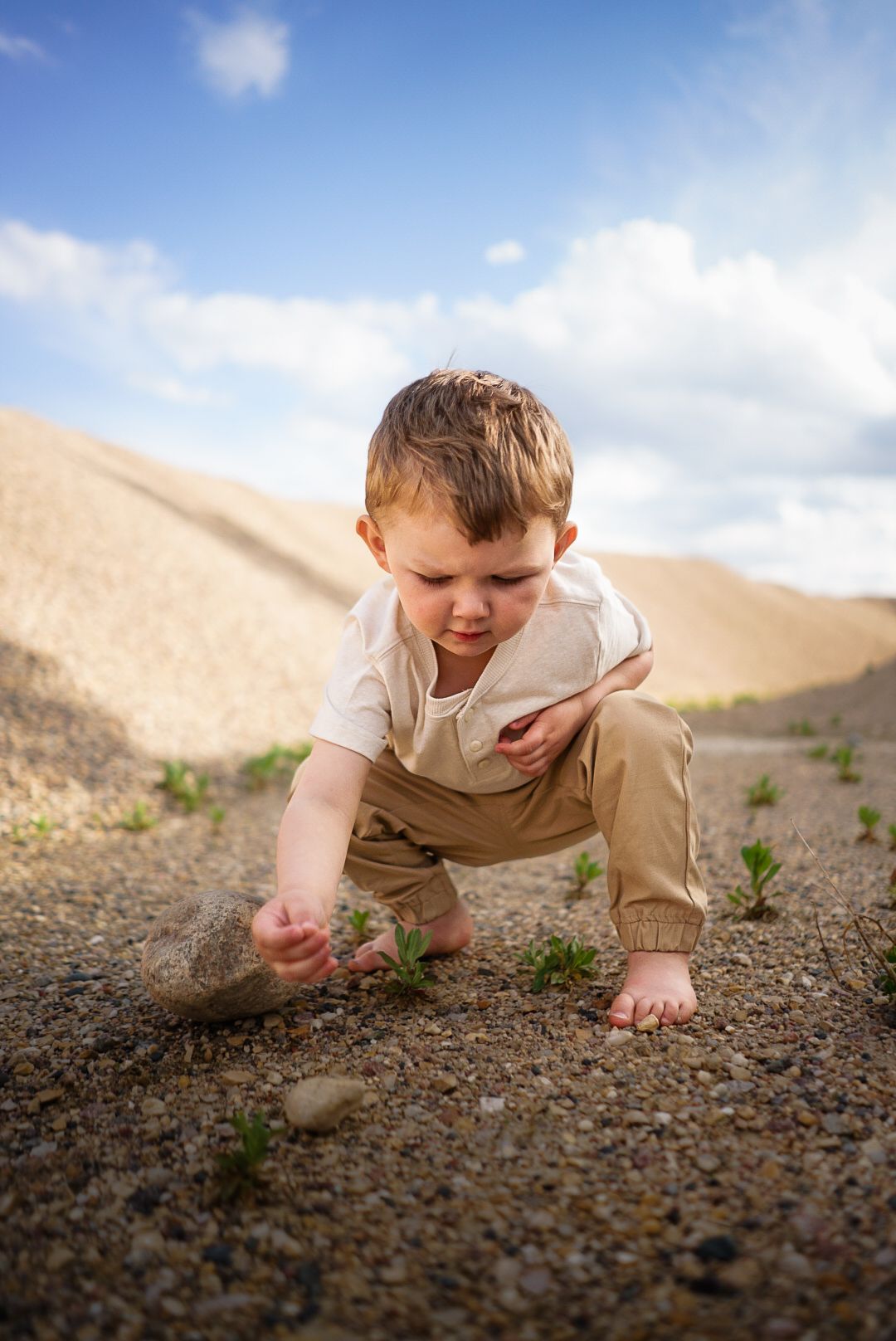 A small child crouches to explore the ground on a desert hill.