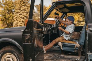 Child climbing into vintage black pickup truck on sunny afternoon.