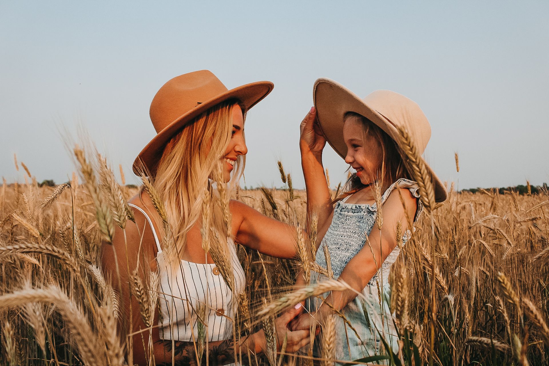 Women in sun hats laughing together in a golden wheat field at sunset.