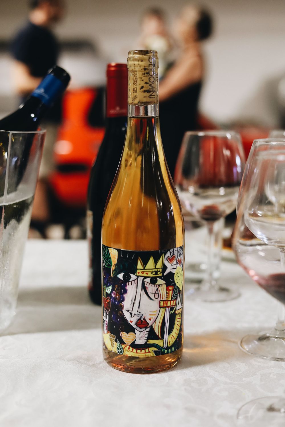 Artistically labeled wine bottles displayed on a white tablecloth at a tasting event.