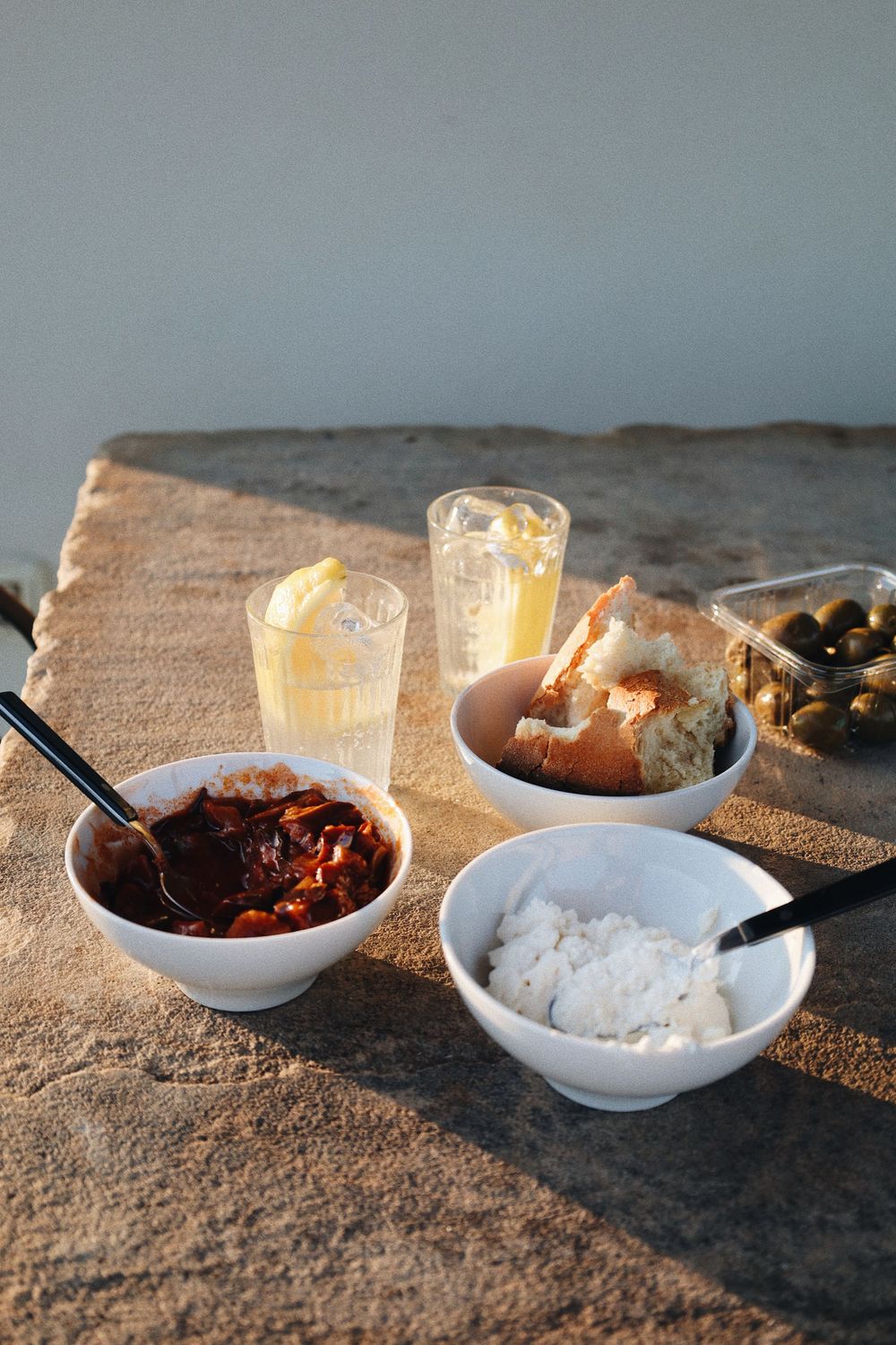 Small white bowls with various ingredients and drinks arranged on a rustic stone surface.