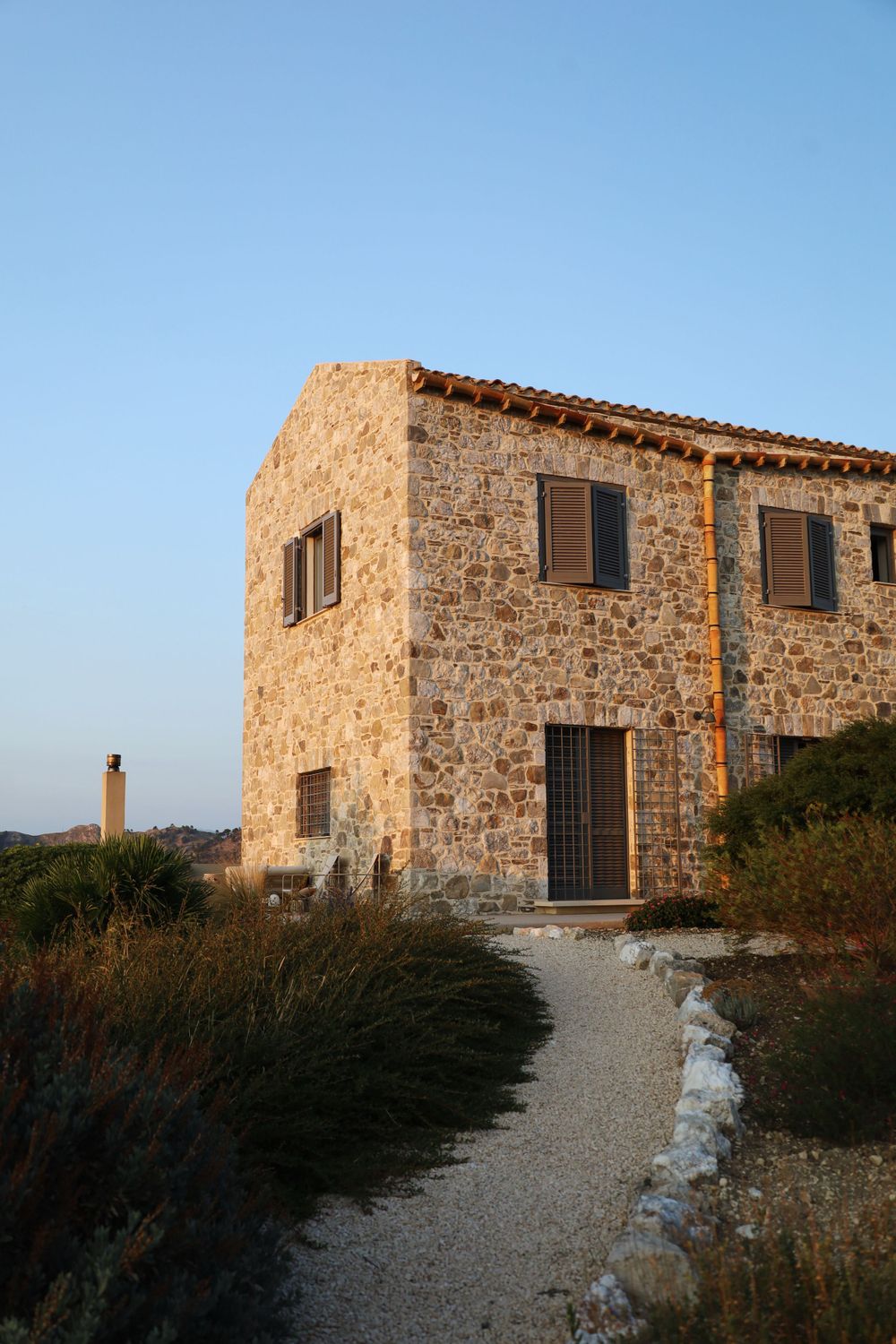Stone building with rustic architecture and shuttered windows against a clear blue sky.
