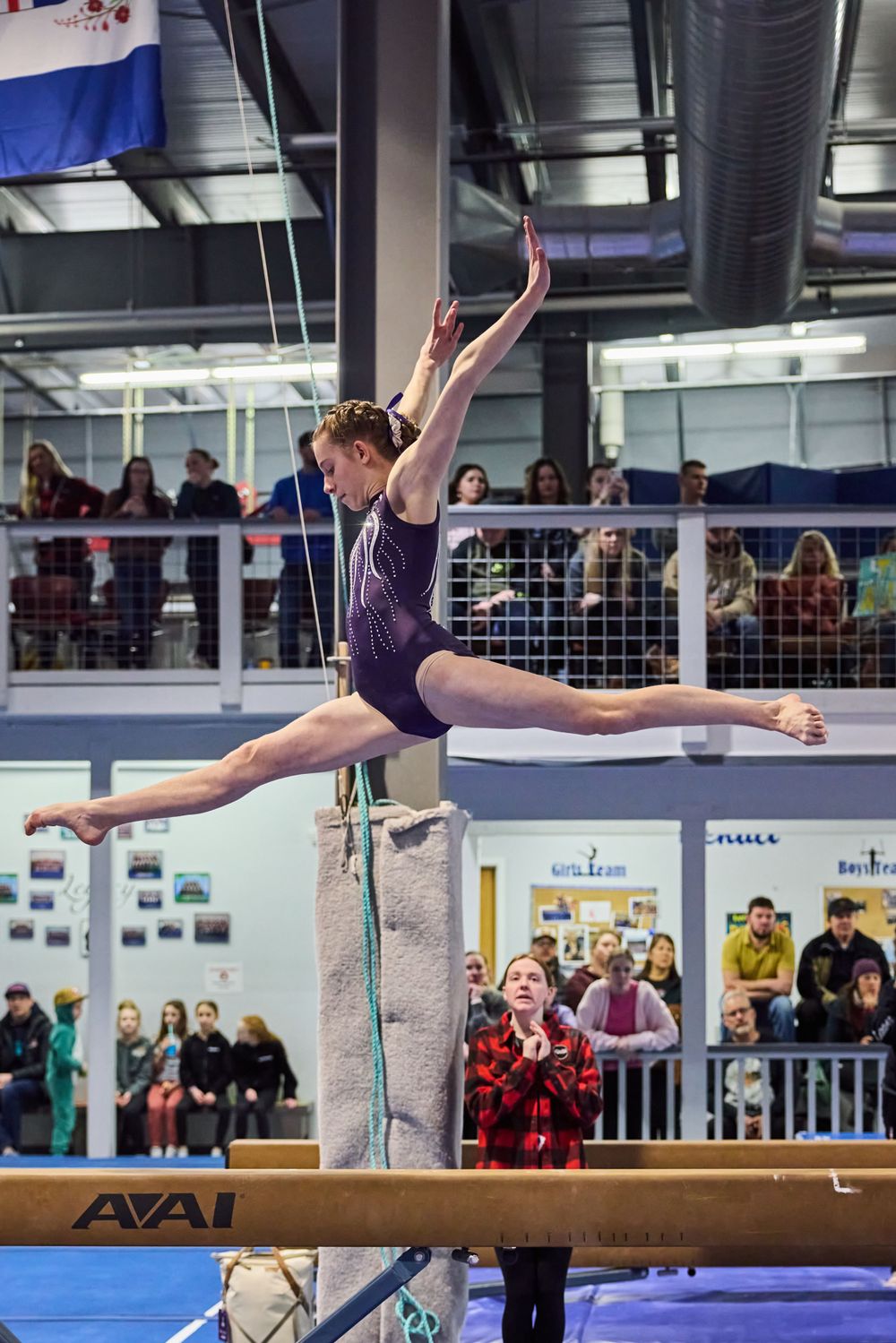 Competitive gymnast executes split position on balance beam during gymnastics meet.