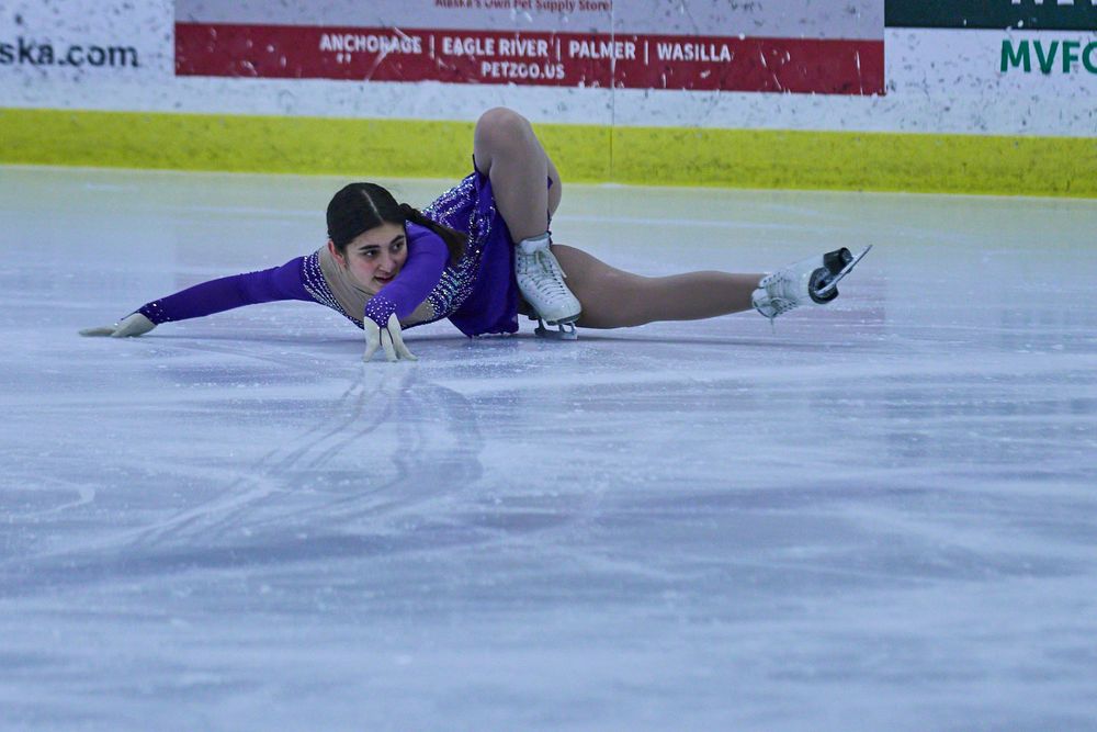 Figure skater in purple outfit slides across ice during performance at competition.