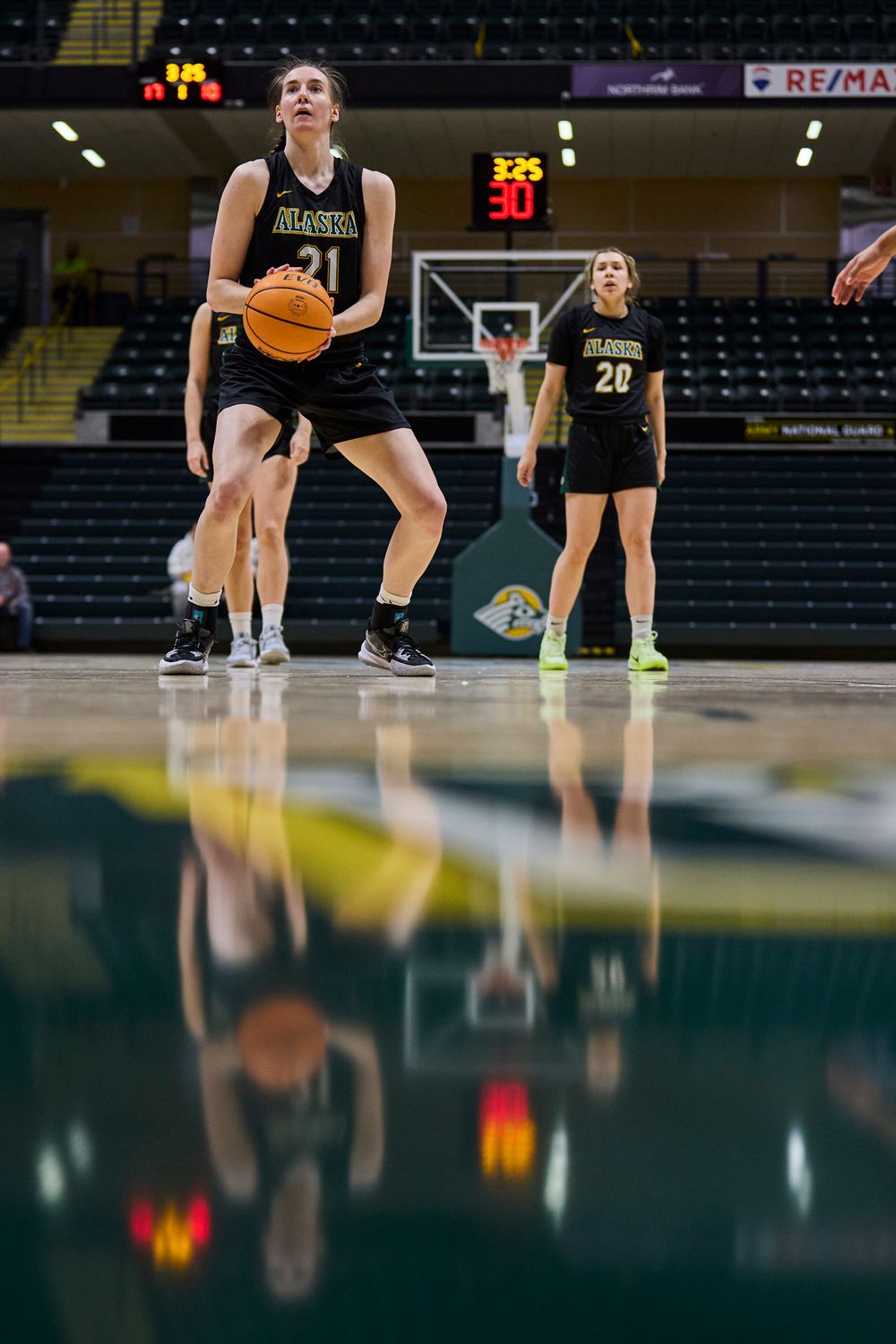 Basketball player in black uniform prepares to take a shot with reflective court surface below.