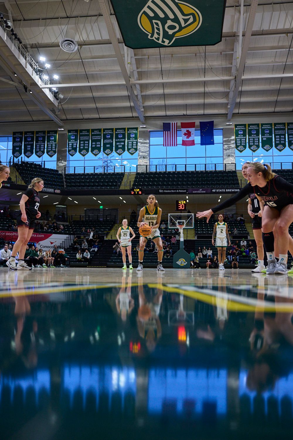 Basketball court with team banners and American flag reflected in polished floor during game.